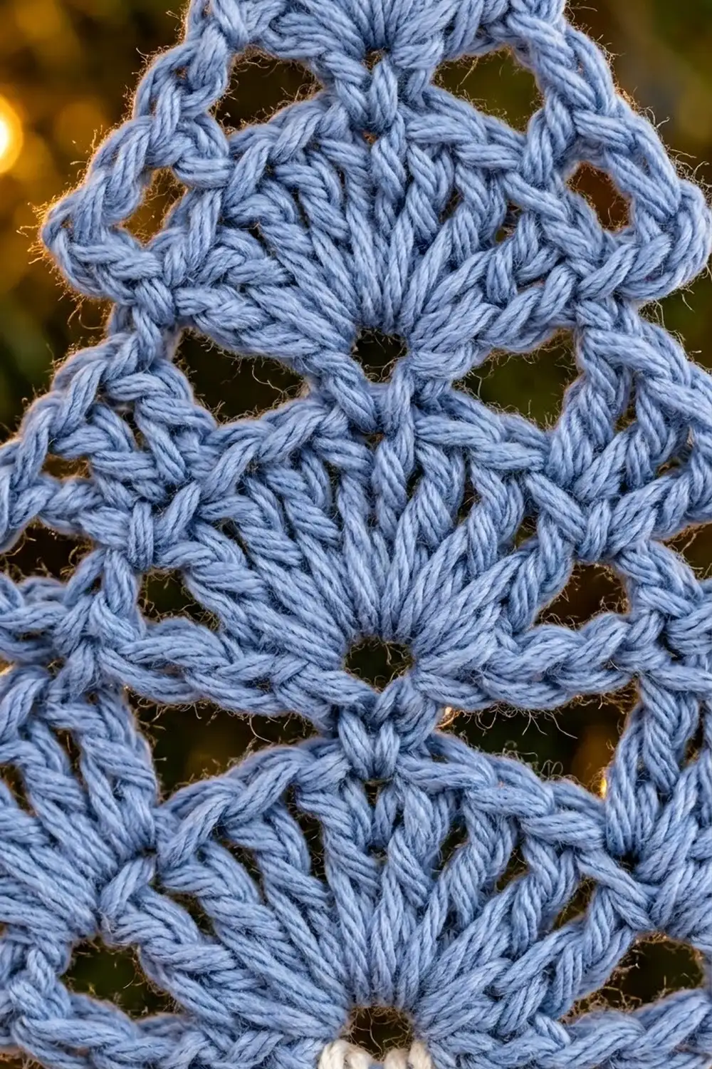 Detailed close-up of periwinkle crochet lace with delicate diamond openwork and warm golden bokeh background.