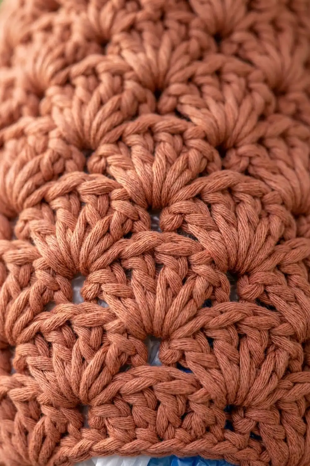 Close-up of warm terracotta crocheted fabric displaying intricate puff stitches with a three-dimensional, textured surface.