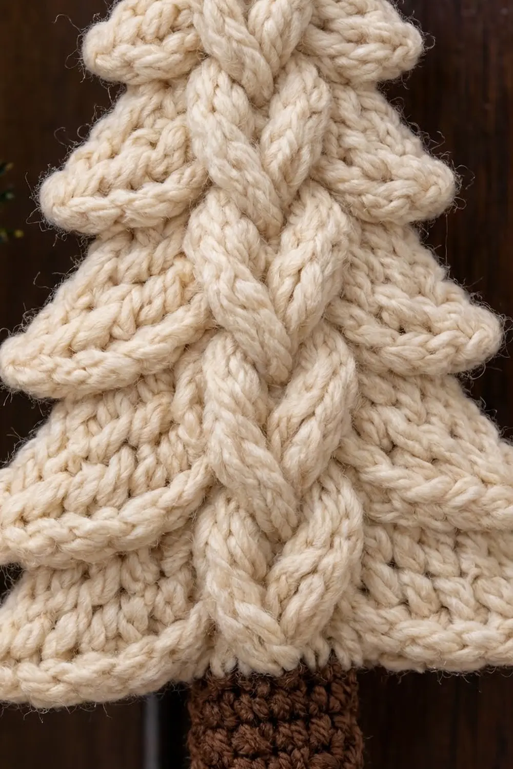 Close-up of cream-colored crocheted Christmas tree with thick cable knit stitching and brown base.