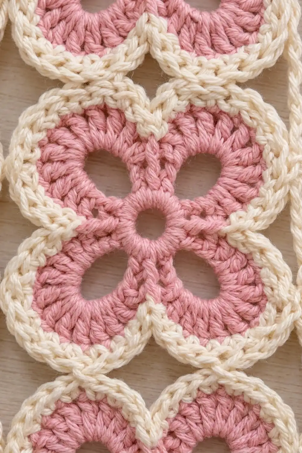 Close-up of crocheted granny squares with pink centers and cream-colored borders arranged in a repeating pattern.