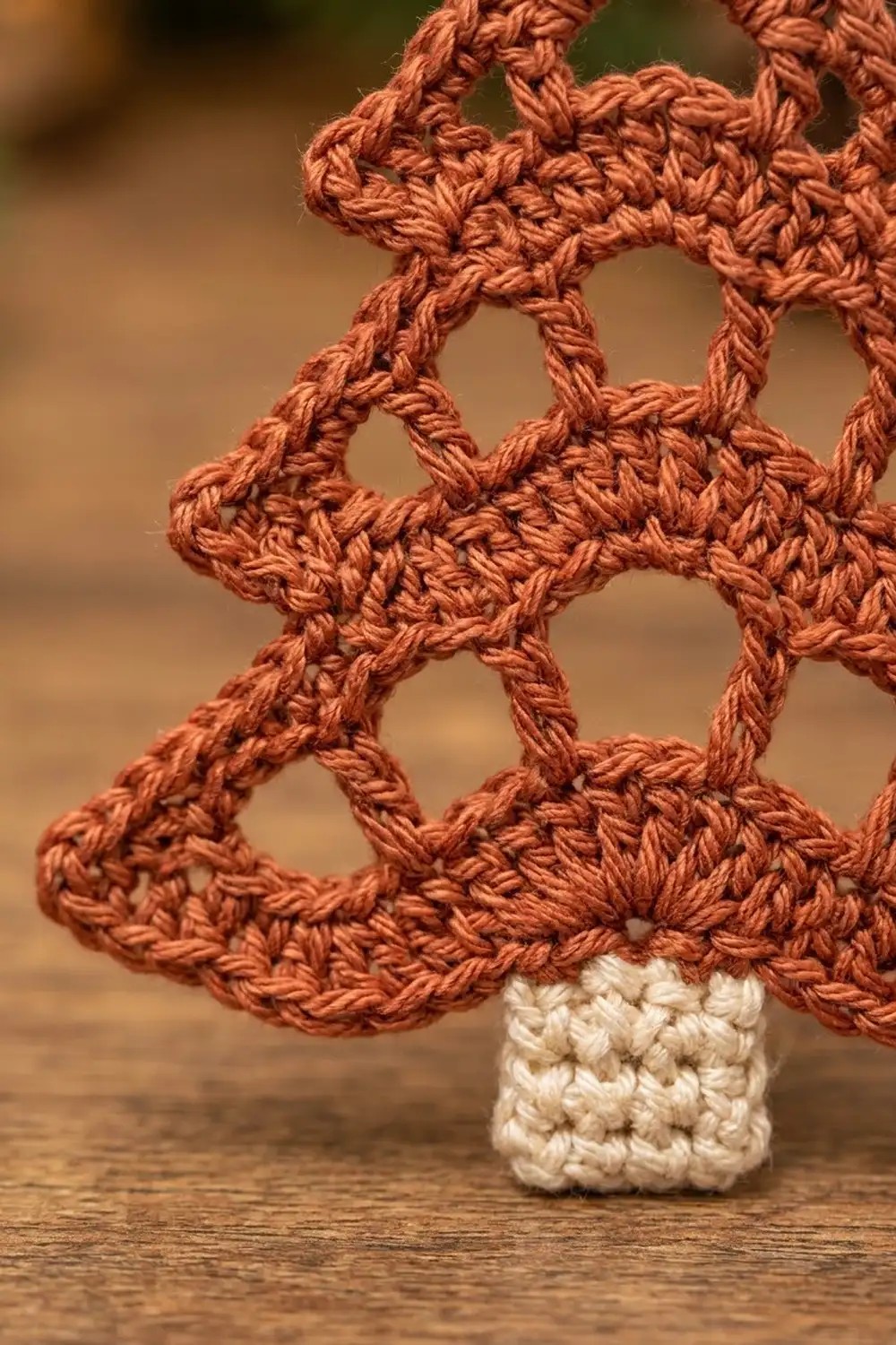 Crocheted rust-orange geometric lattice with cream base on wooden surface, blurred neutral background behind.