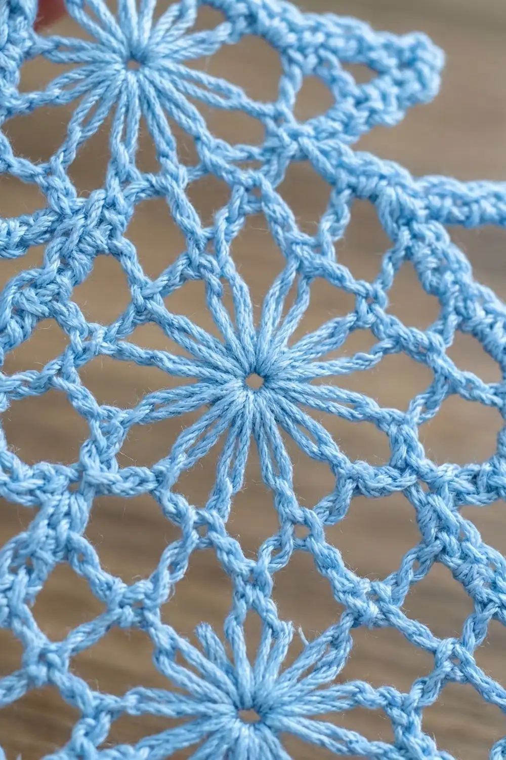 Light blue crochet featuring six-petaled star flowers connected by twisted yarn strands in geometric pattern.