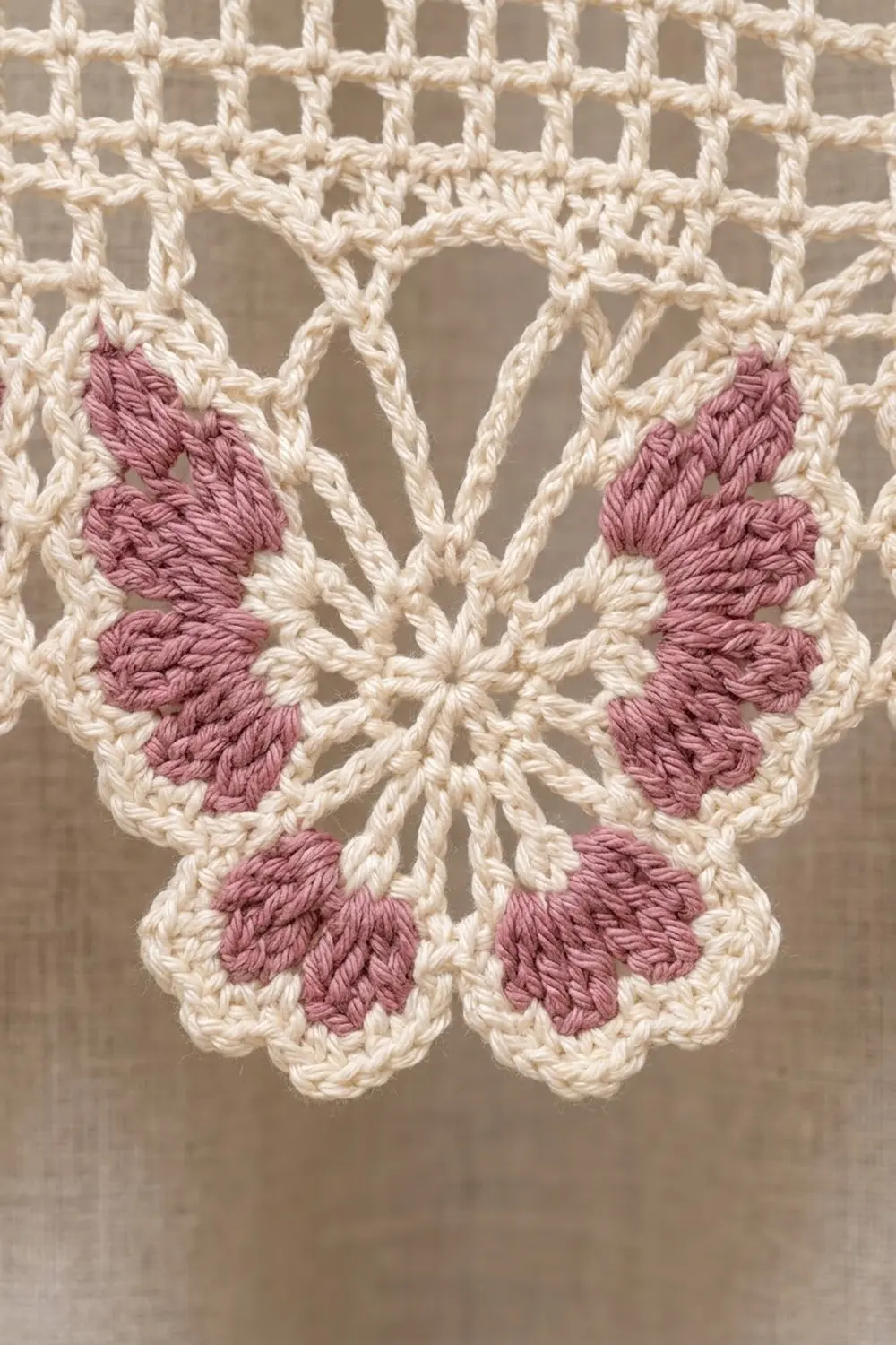 Crocheted butterfly motif with pink filled wings and cream-colored openwork lace detail against neutral background.