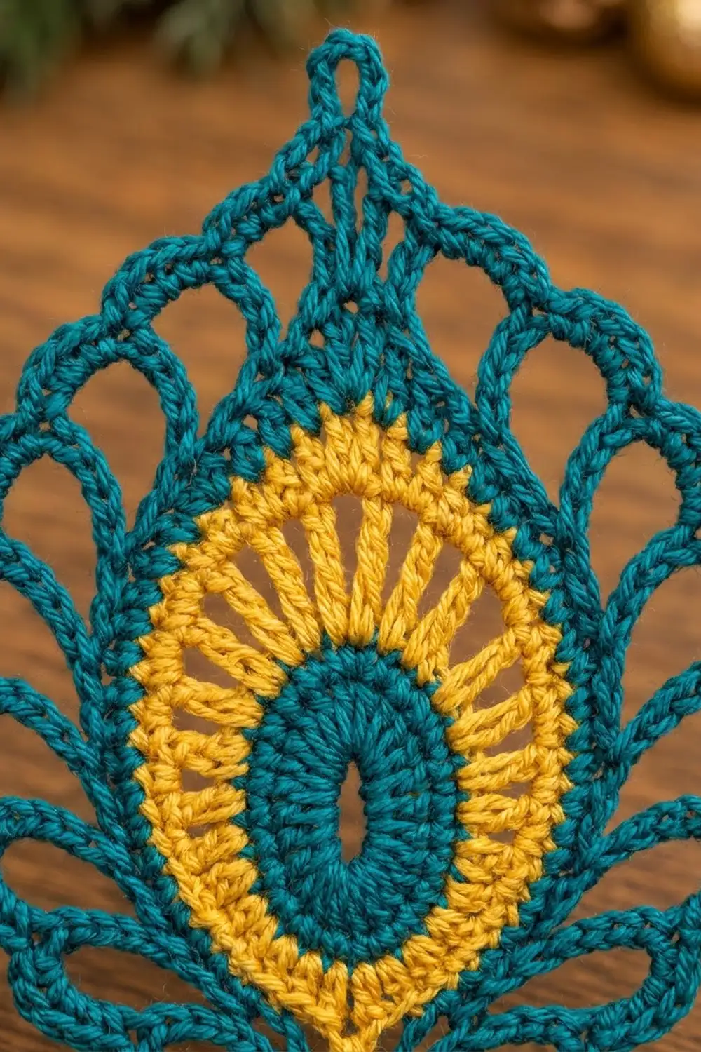 Close-up of a crocheted ornament featuring teal yarn forming a leaf shape with a golden yellow center detail.