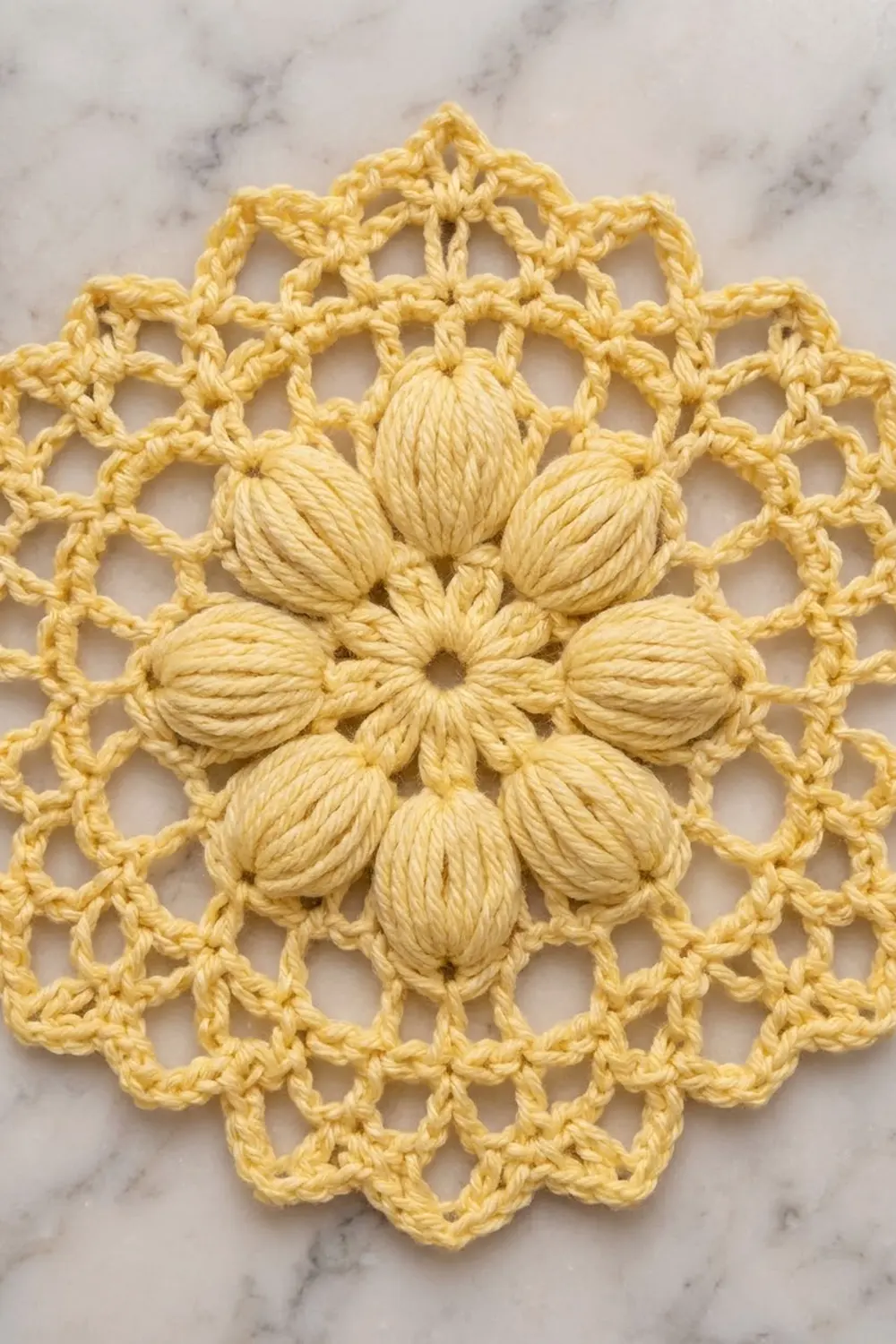 A yellow crochet doily with a dimensional flower motif in the center, displayed on a marble surface.