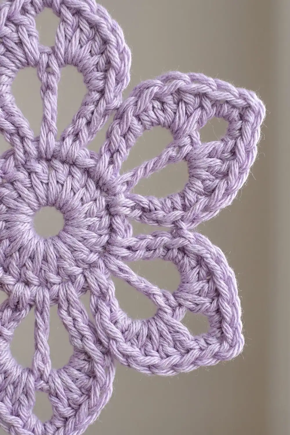 Close-up of lavender purple crocheted lace fabric with openwork loops against a neutral beige background.