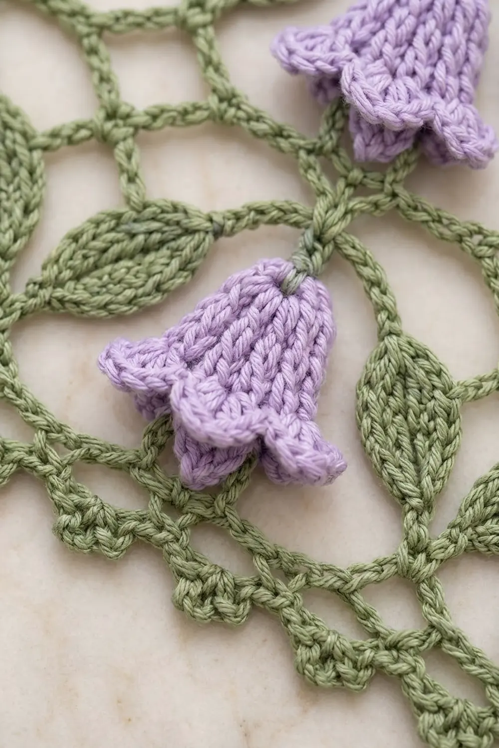 Purple crocheted flowers with green leaves arranged on a white textured background.