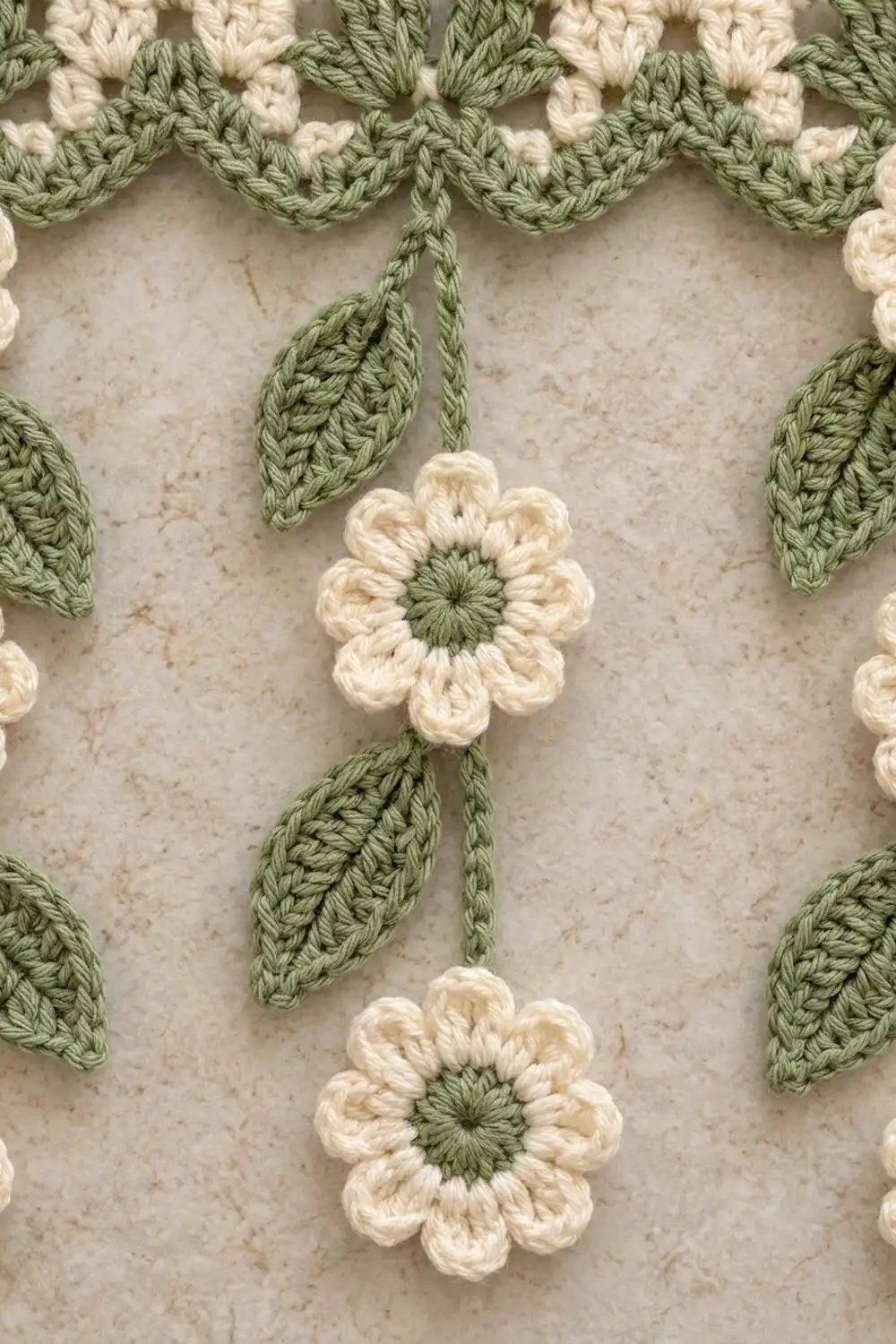Crocheted flowers with cream petals and sage green centers hanging from matching green stems and leaves.