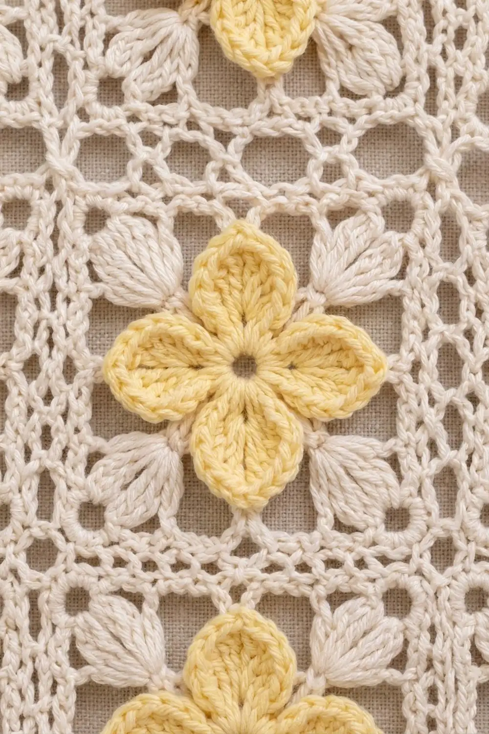 Crocheted lace fabric with cream-colored geometric pattern and yellow four-petal flowers on neutral background.