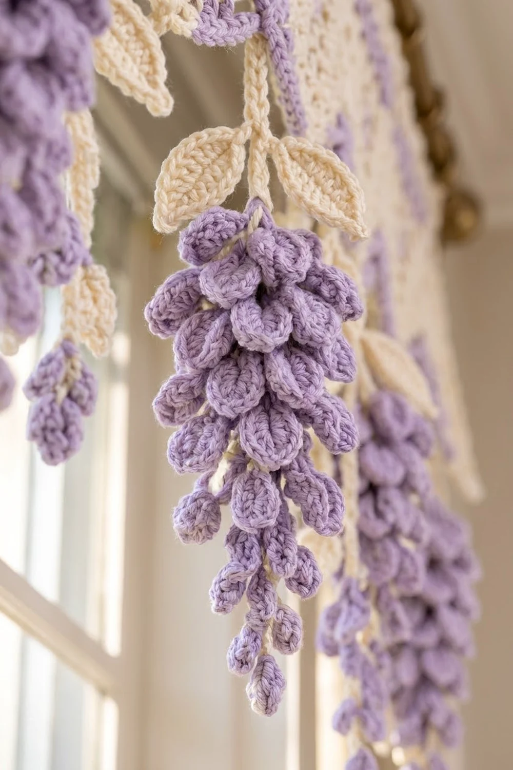 Crocheted lavender flowers with cream-colored leaves hanging as delicate handmade decorations against a soft, blurred background.