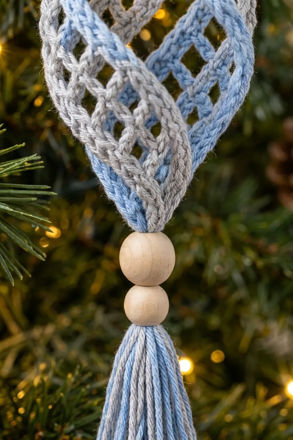 A decorative ornament made of two wooden beads and blue-gray braided ribbon hanging on an evergreen branch.