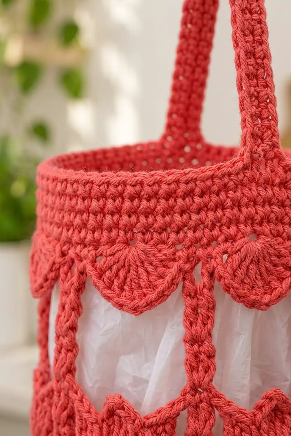 Close-up of a coral crochet tote bag with scalloped trim and white lining, displayed outdoors.