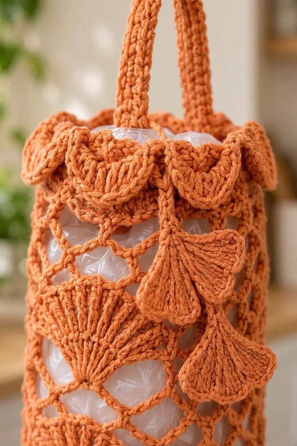 Close-up of an orange crocheted macramé plant hanger with decorative leaf appliqués holding a white pot.