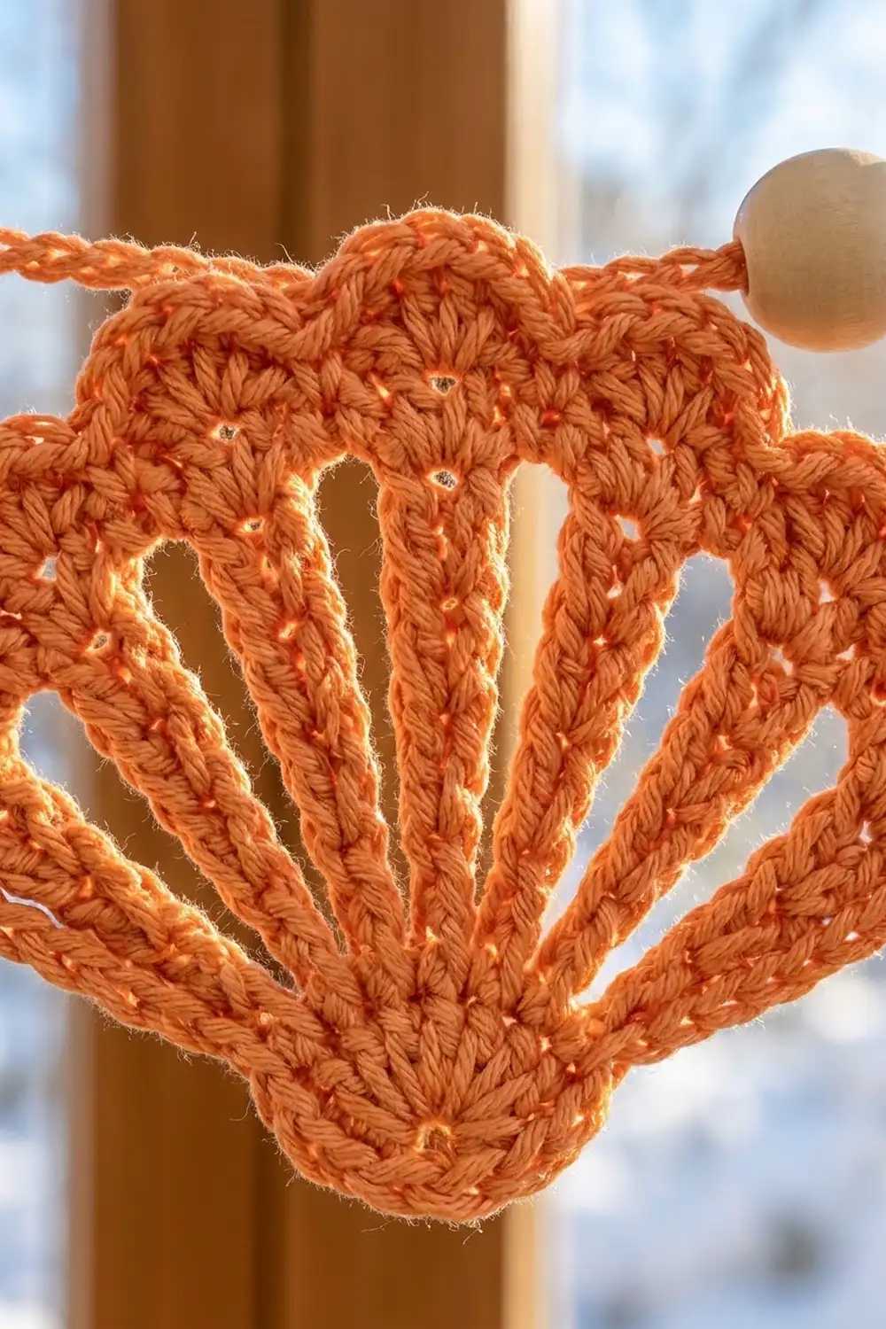 A crocheted orange octopus ornament with beaded eyes hangs from a twisted rope against a blurred indoor background.