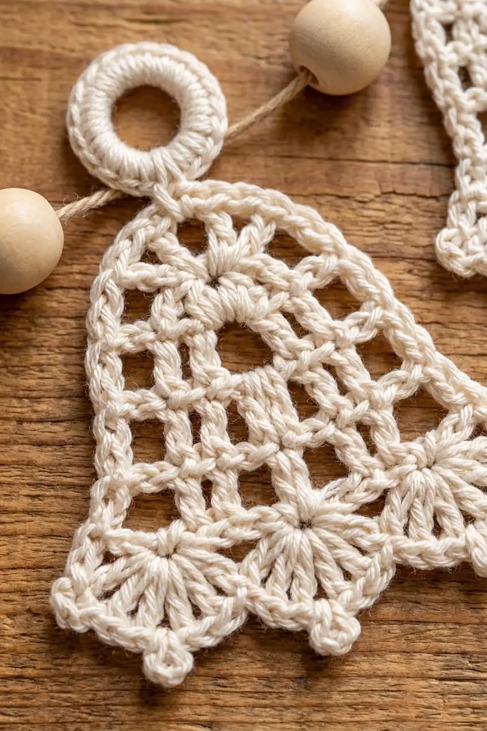 Crocheted cream-colored ornament with open lattice pattern and wooden bead, displayed on wooden surface.