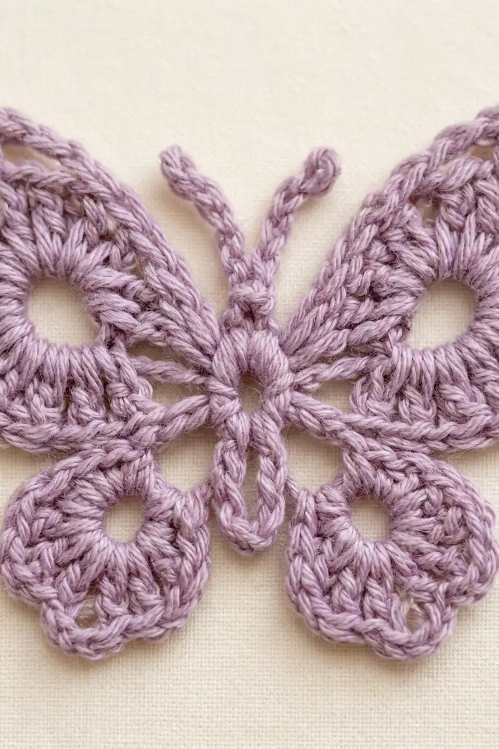 Lavender crochet butterfly appliqué with detailed lacework wings displayed on cream-colored fabric background.