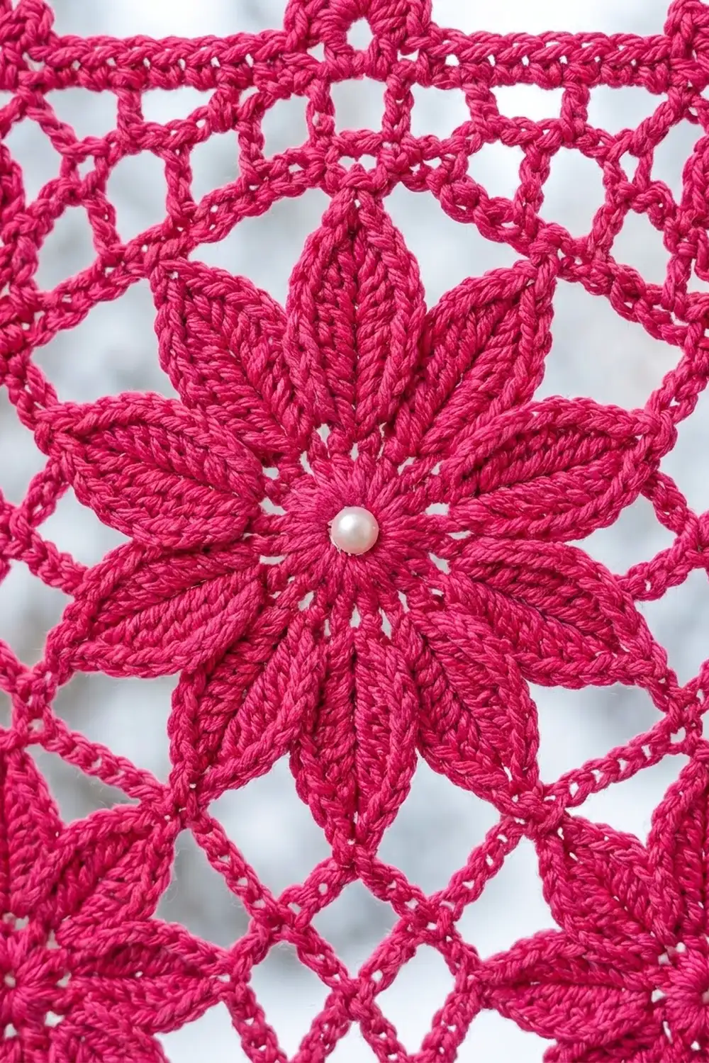 Bright pink crocheted flower with pearl center embellishment and openwork lace pattern against white background.