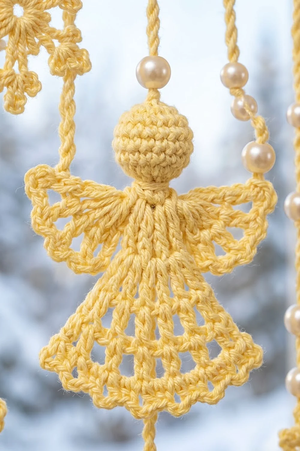 A golden crocheted angel ornament with pearl beads hanging from twisted yarn strings against a snowy background.