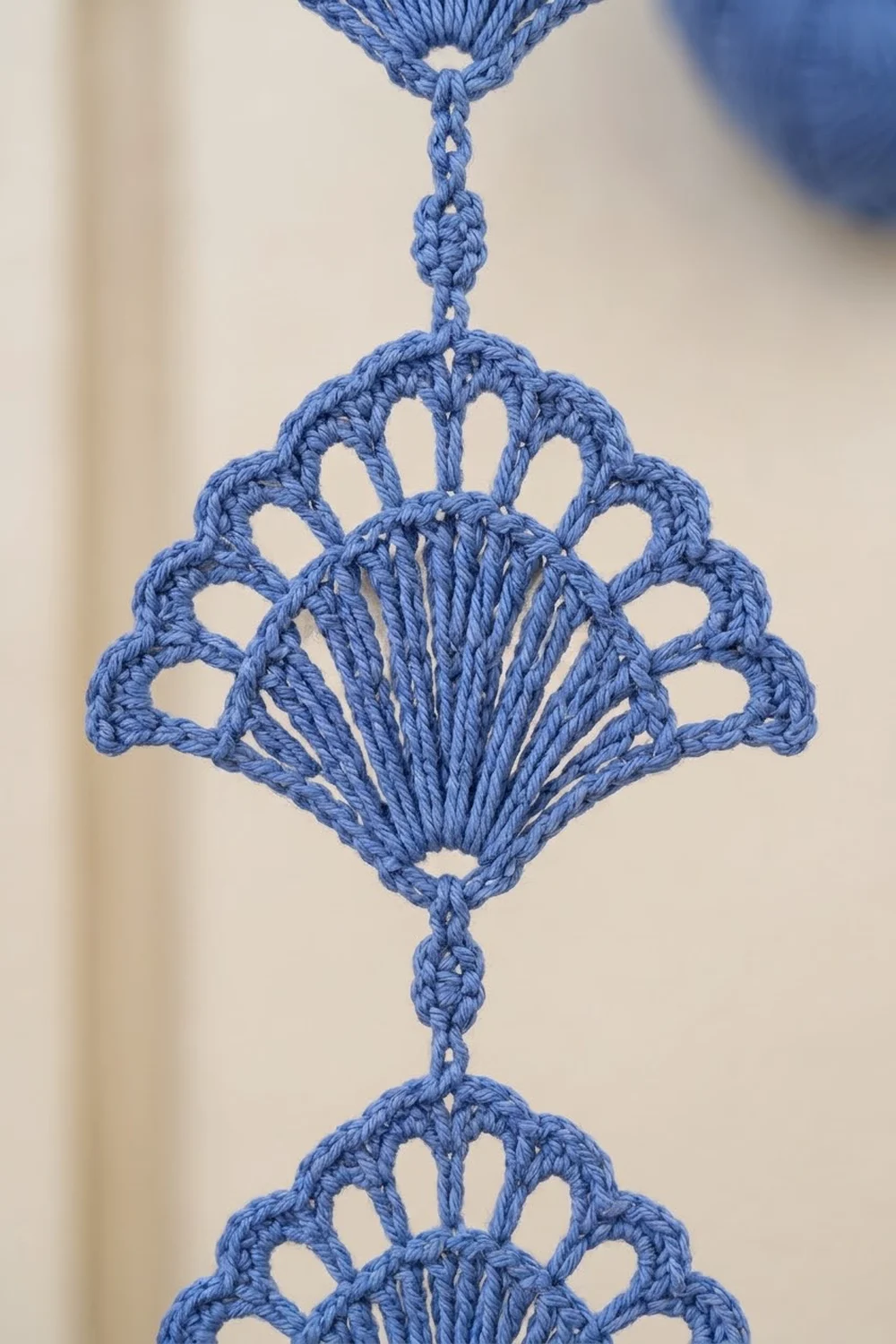Blue crocheted lace ornament featuring a fan-shaped design with decorative connecting chains against a neutral background.