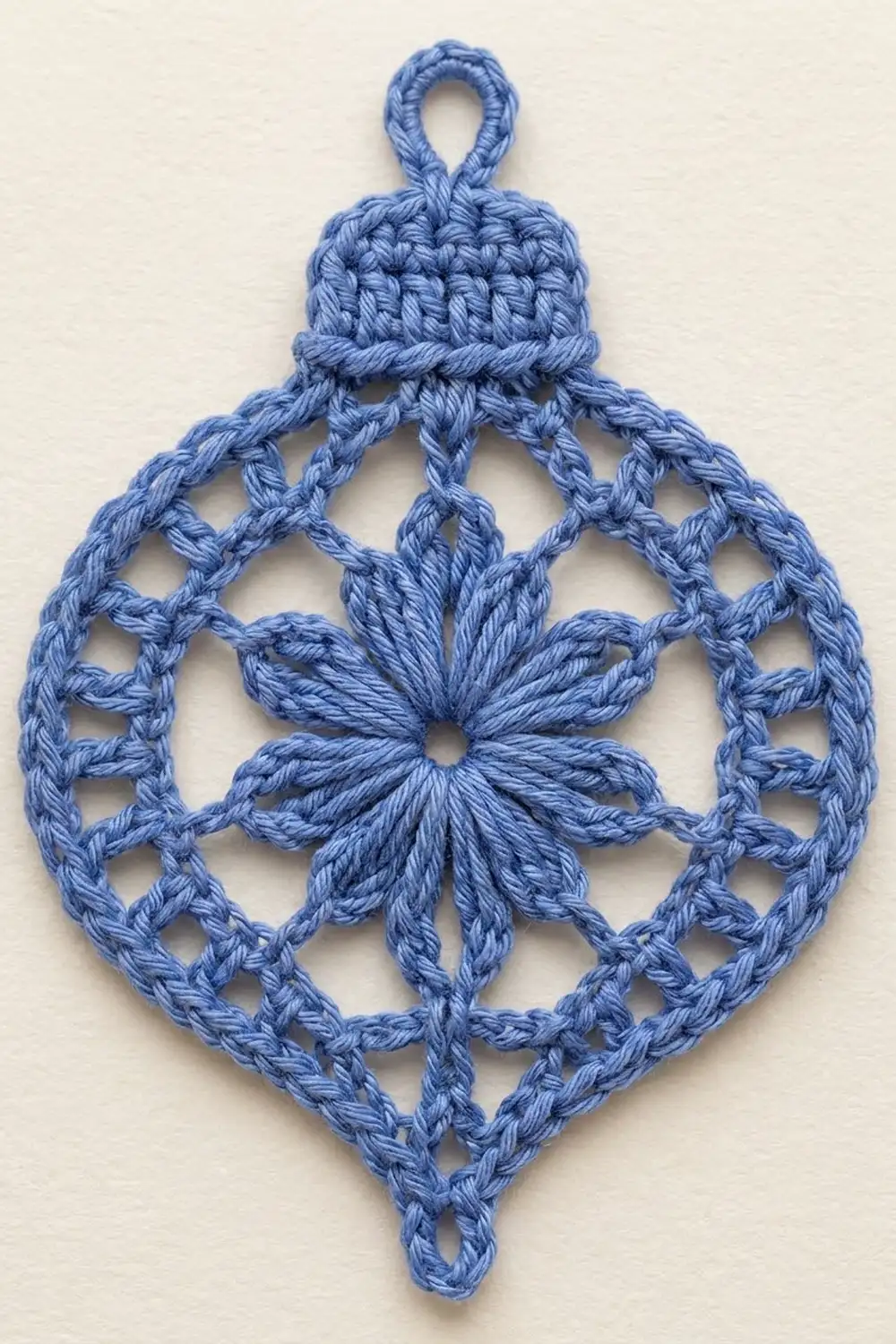 A blue crocheted ornament with a diamond shape, featuring an eight-pointed star center and lattice pattern design.