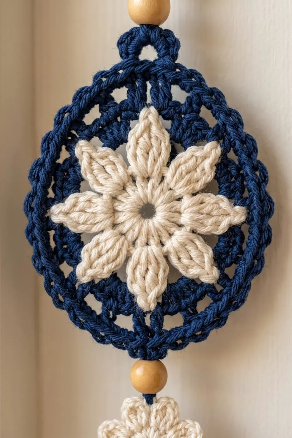 Navy blue crocheted ornament with cream star center and wooden beads on neutral background.