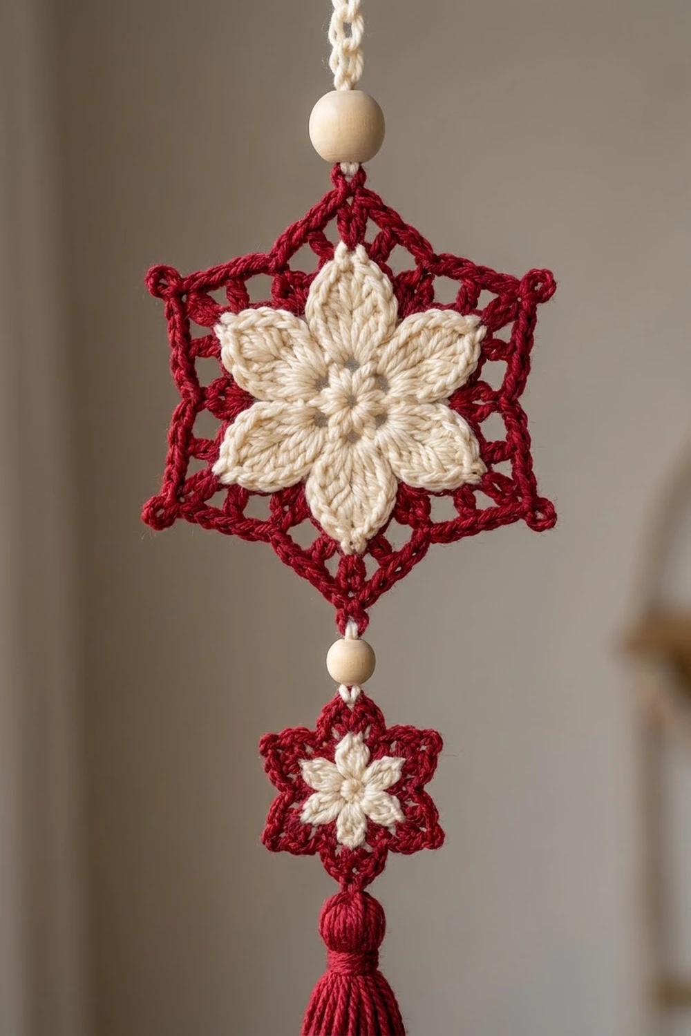 A red and cream crocheted snowflake ornament with wooden beads hanging from a twisted cord.
