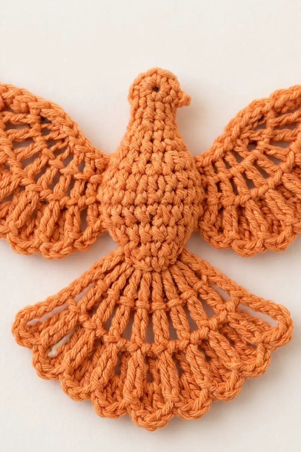 Orange crocheted bird ornament with spread wings and detailed lacework against a white background.