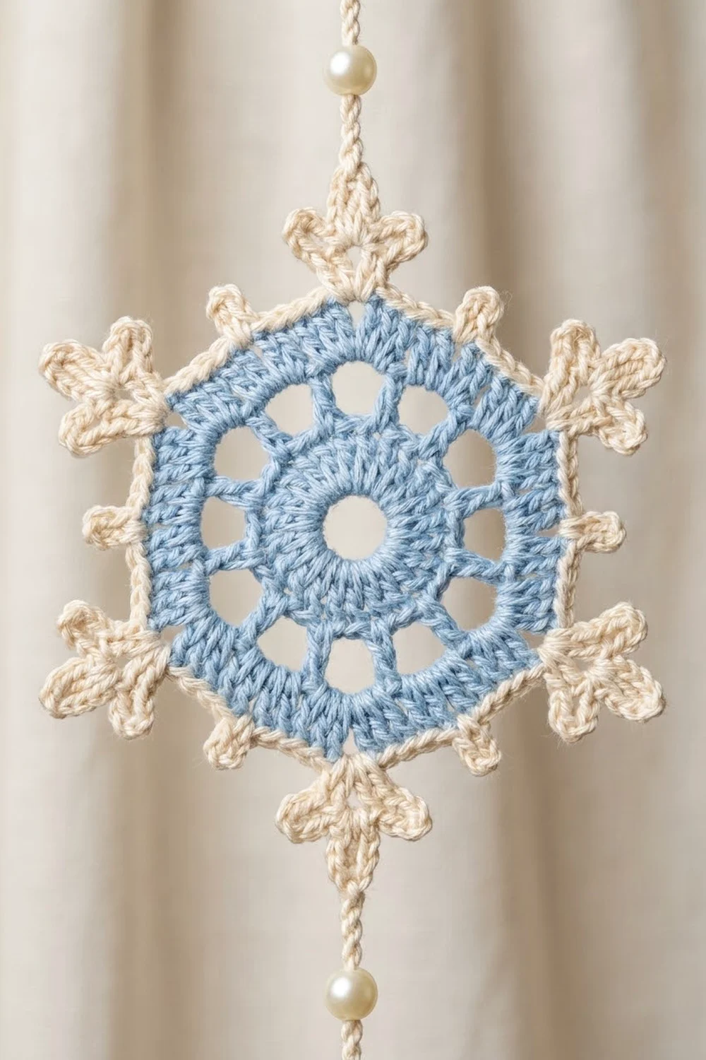 A crocheted snowflake ornament with blue center and cream decorative points, adorned with pearl beads.