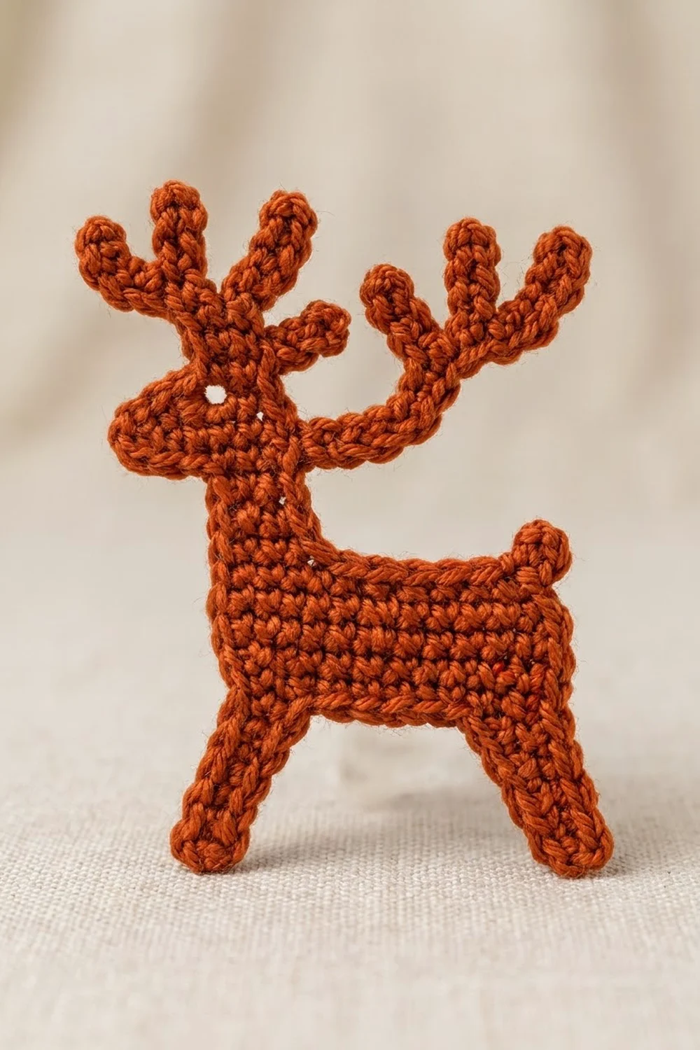 A handmade orange crocheted cactus figurine with multiple arms standing on a neutral beige fabric surface.