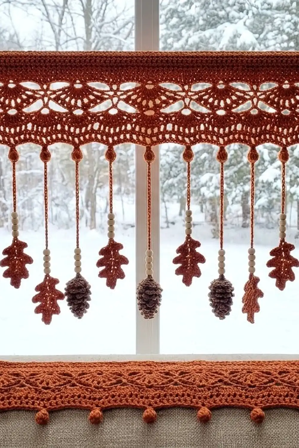 Crocheted rust-colored lace valance with dangling oak leaves and pinecones hanging in a snowy winter window.
