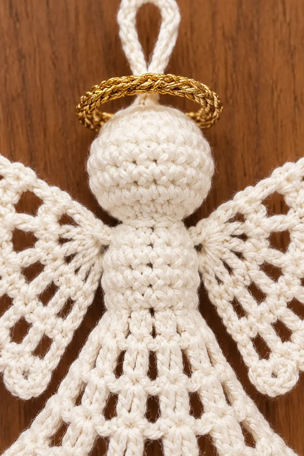 Crocheted white angel ornament with gold halo and hanging loop displayed against wooden background.