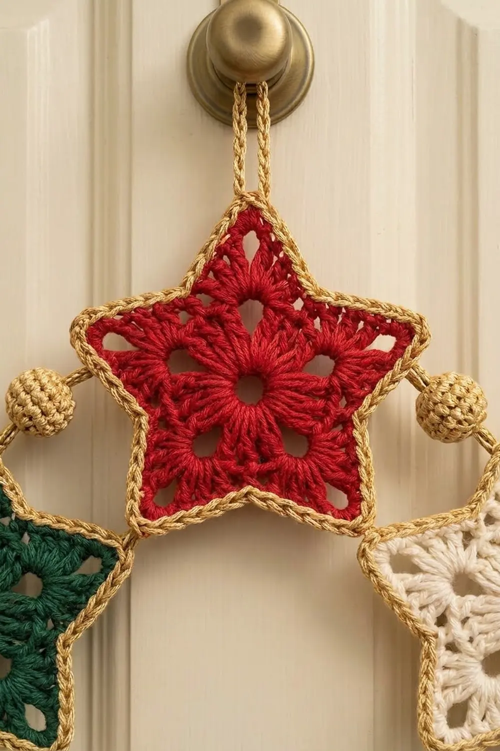 Crocheted red star ornament with gold rope trim hanging from brass hook with matching decorative balls.