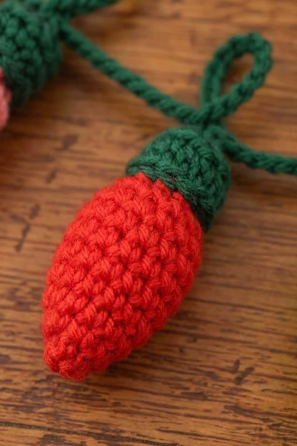 A crocheted red strawberry with green leaf details lying on a wooden surface.