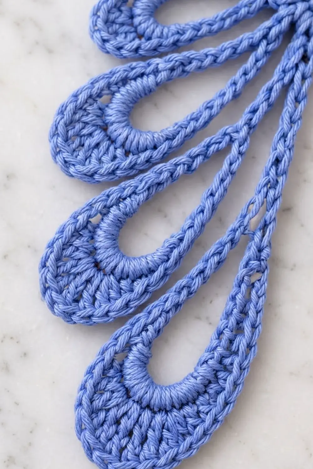 Close-up of blue crocheted loops and braided cord details on a white marble surface.
