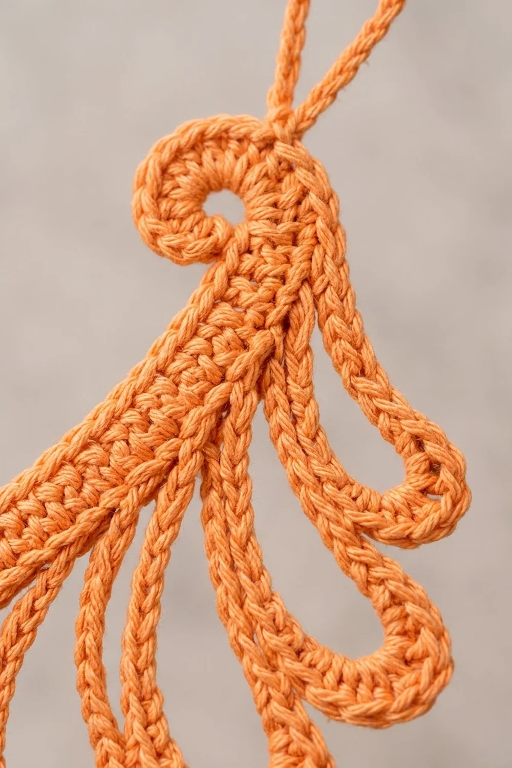 Close-up of an orange braided rope arranged in loops against a neutral gray background.