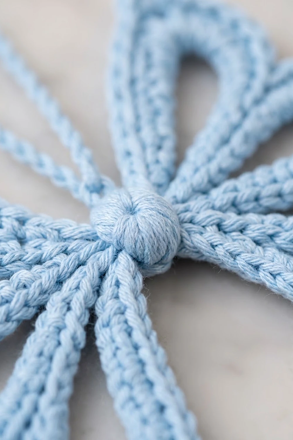 Close-up of a light blue braided rope knot tied in the center against a blurred neutral background.