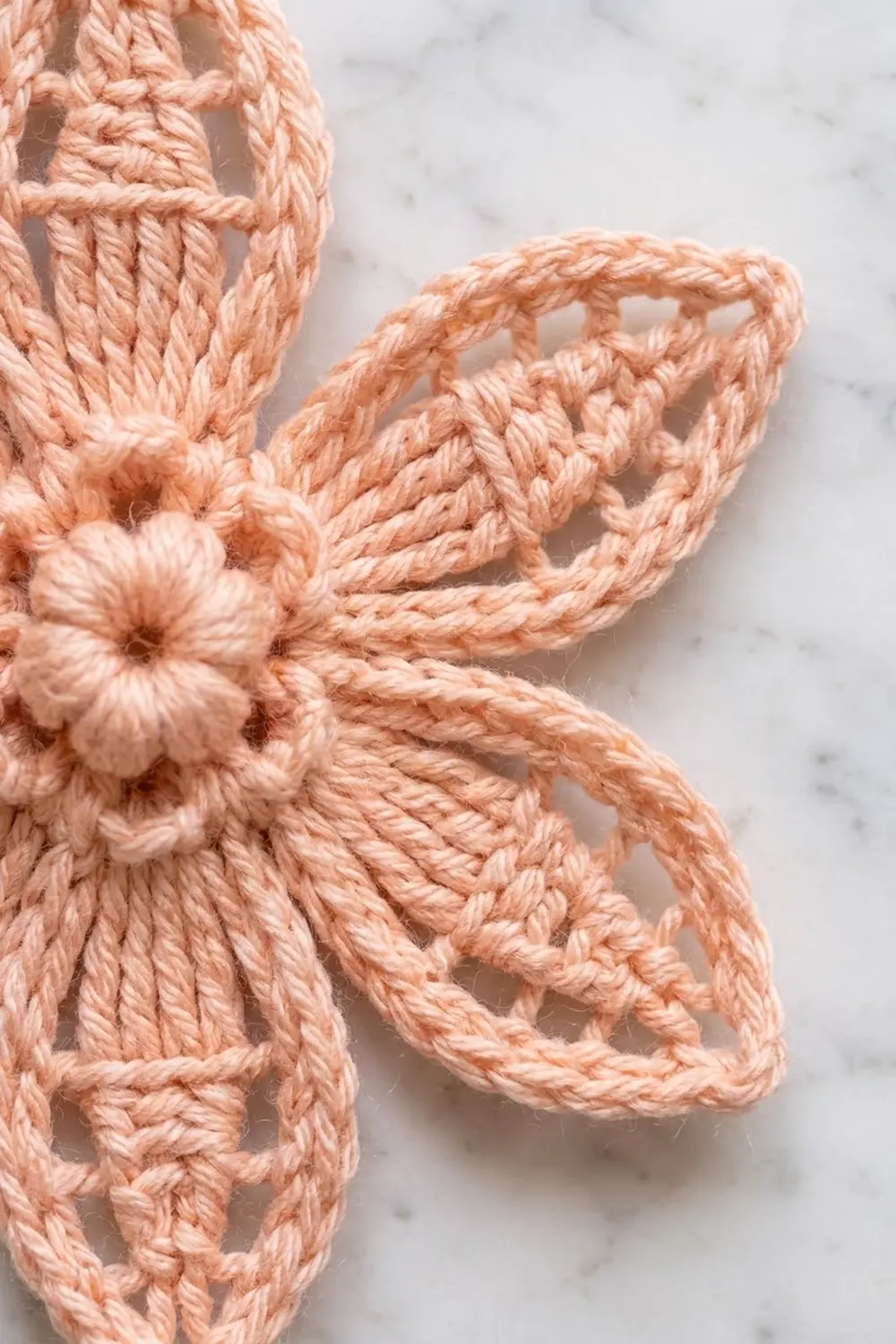 Peach-colored crocheted butterfly with detailed wings and flower center on marble surface.
