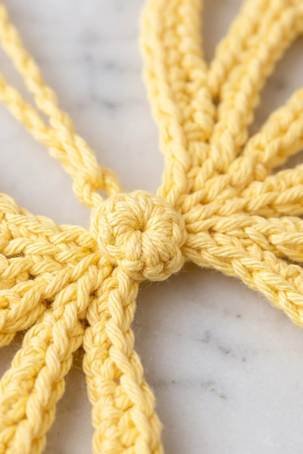 Close-up of a yellow twisted rope knot tied at the center with four strands radiating outward on a light background.