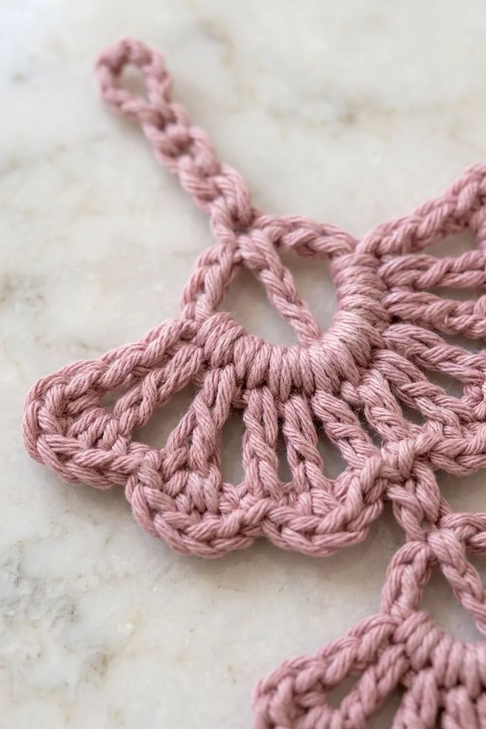 Close-up of delicate pink macramé trim with twisted knots displayed on a light marble surface.