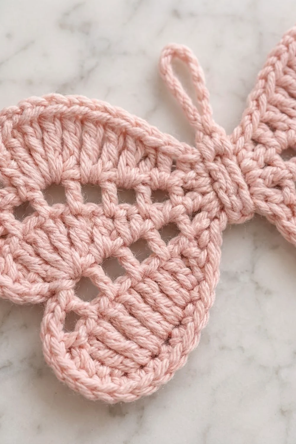 A pink crocheted bunny ear ornament with open lacework detail displayed on a marble surface.
