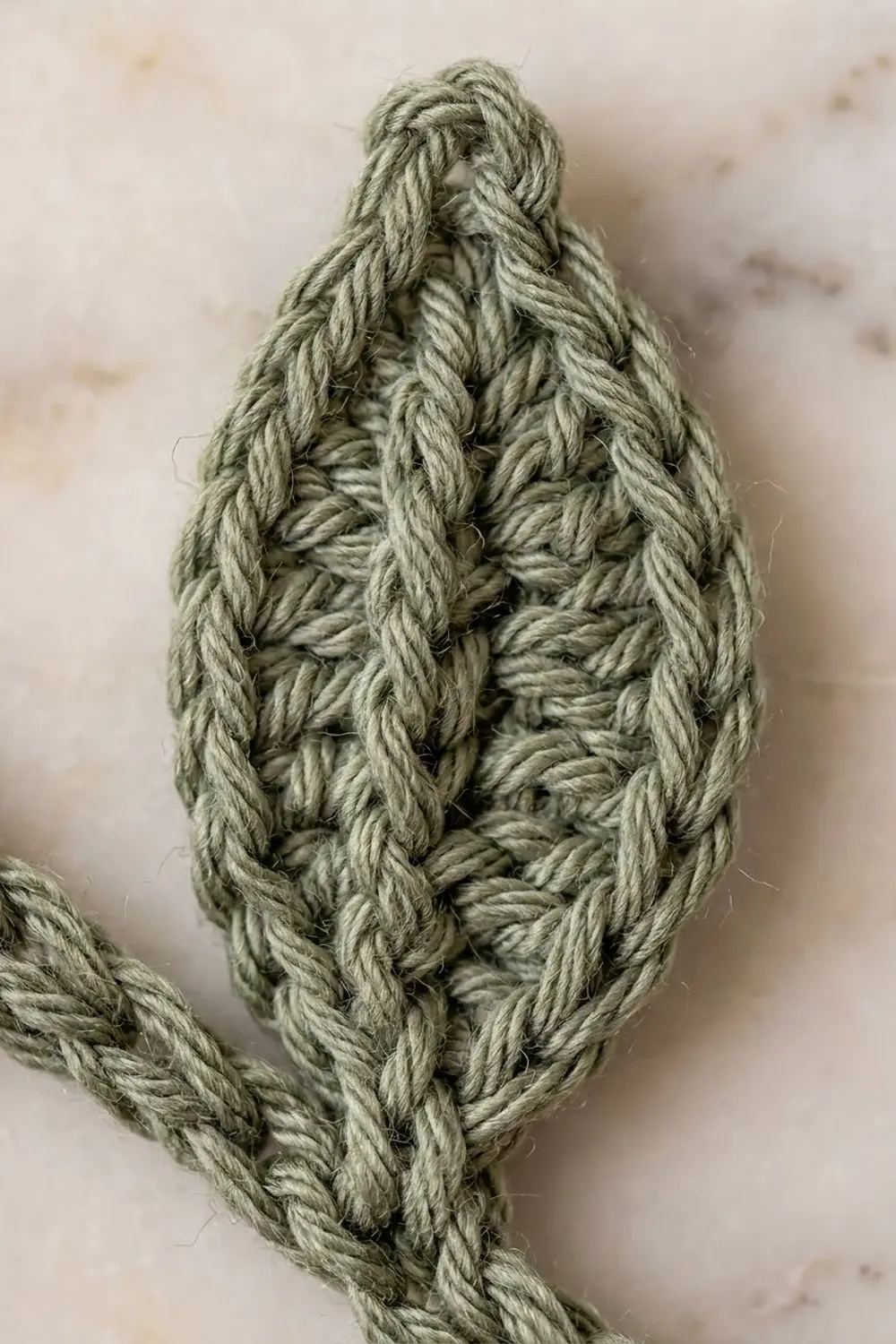 Close-up of a twisted sage green rope knot against a neutral beige textured background.