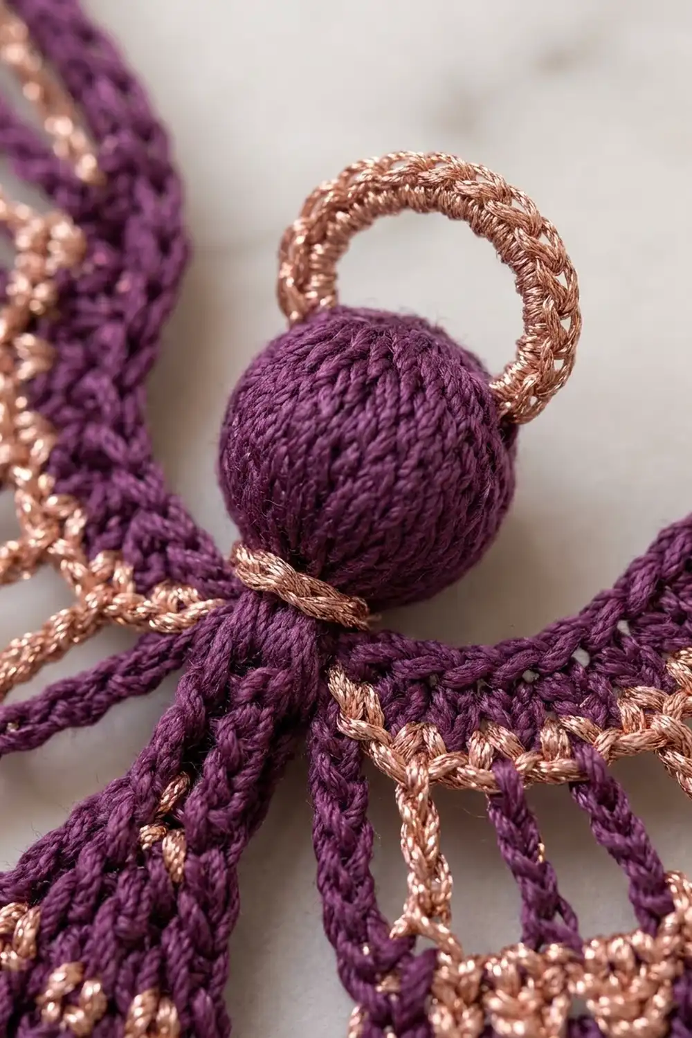 Close-up of a purple and rose gold decorative tassel with braided cords and a wrapped spherical ball detail.