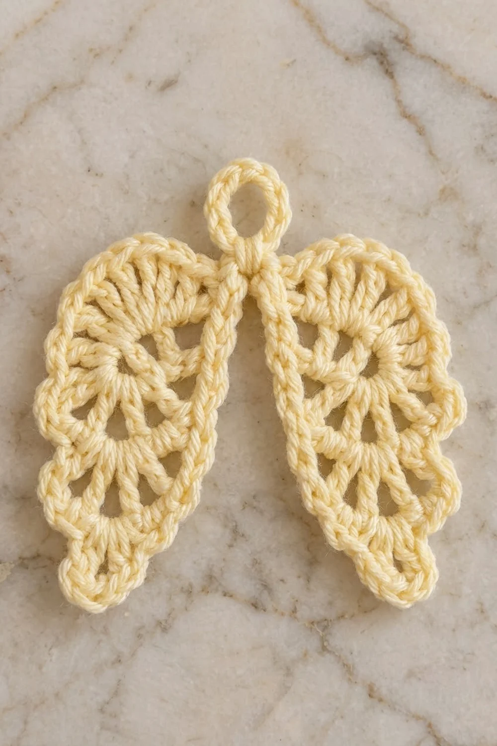 A pair of cream-colored crocheted wing ornaments with an open lacework pattern on a marble surface.