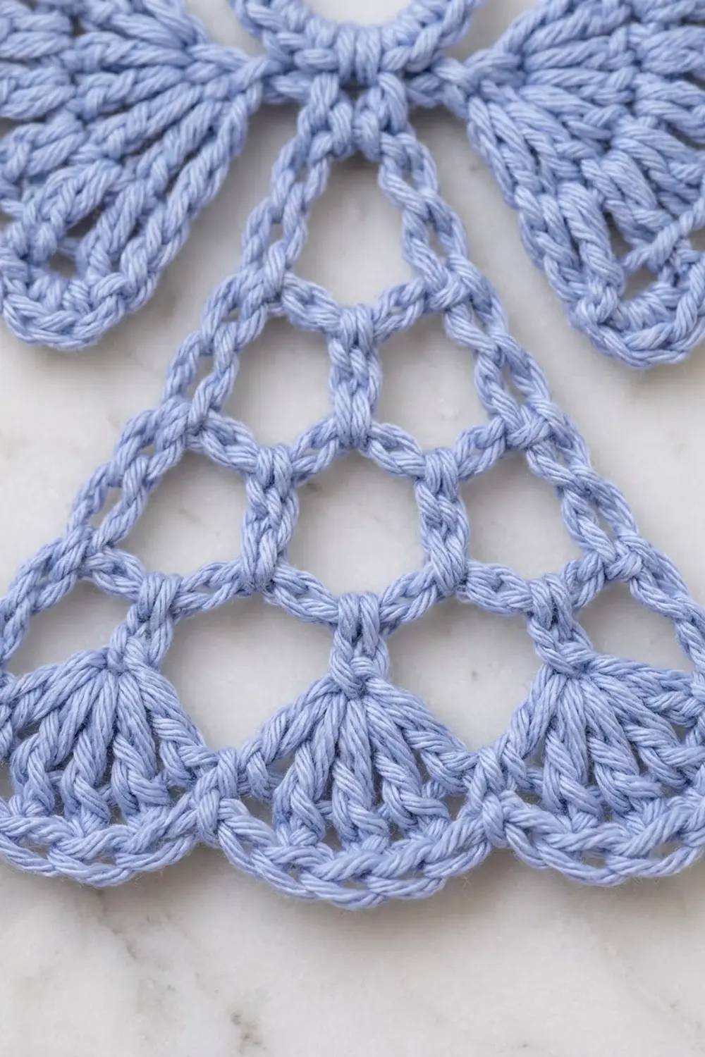 Close-up of delicate light blue crocheted lace trim with scalloped edges on white background.