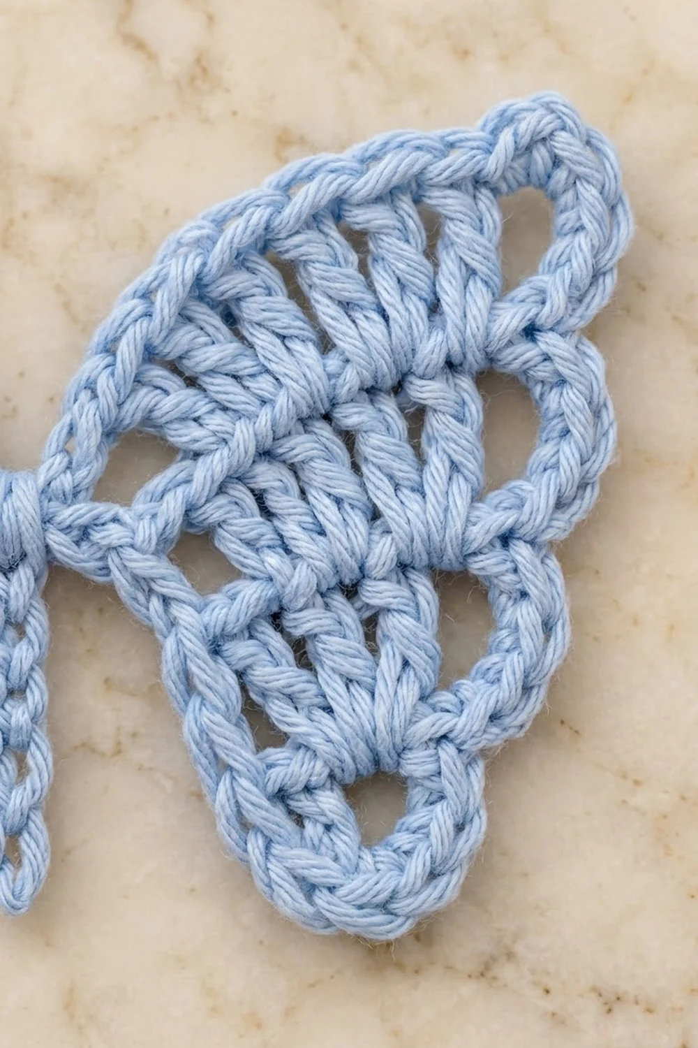 Light blue braided rope with decorative knots displayed on a beige marble textured surface.