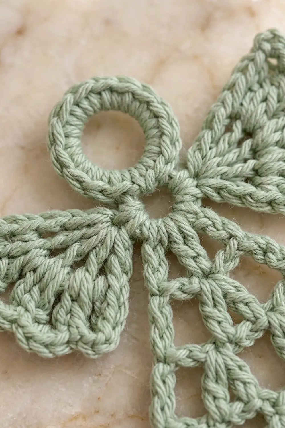 A pale sage green twisted rope forms an decorative knot pattern against a cream-colored textured background.