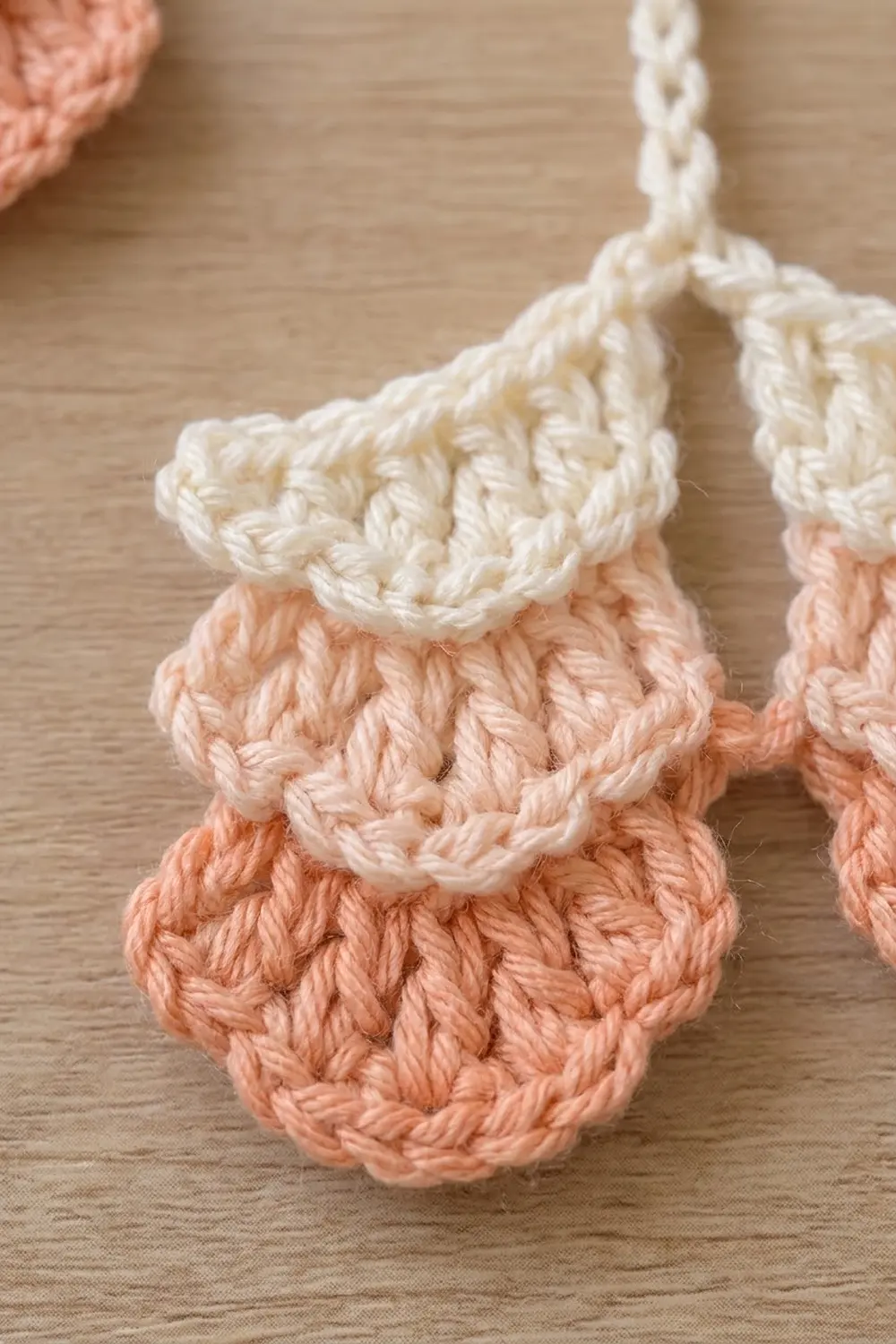 Close-up of crocheted ornaments in cream and peach colors hanging from white chains on a wooden surface.