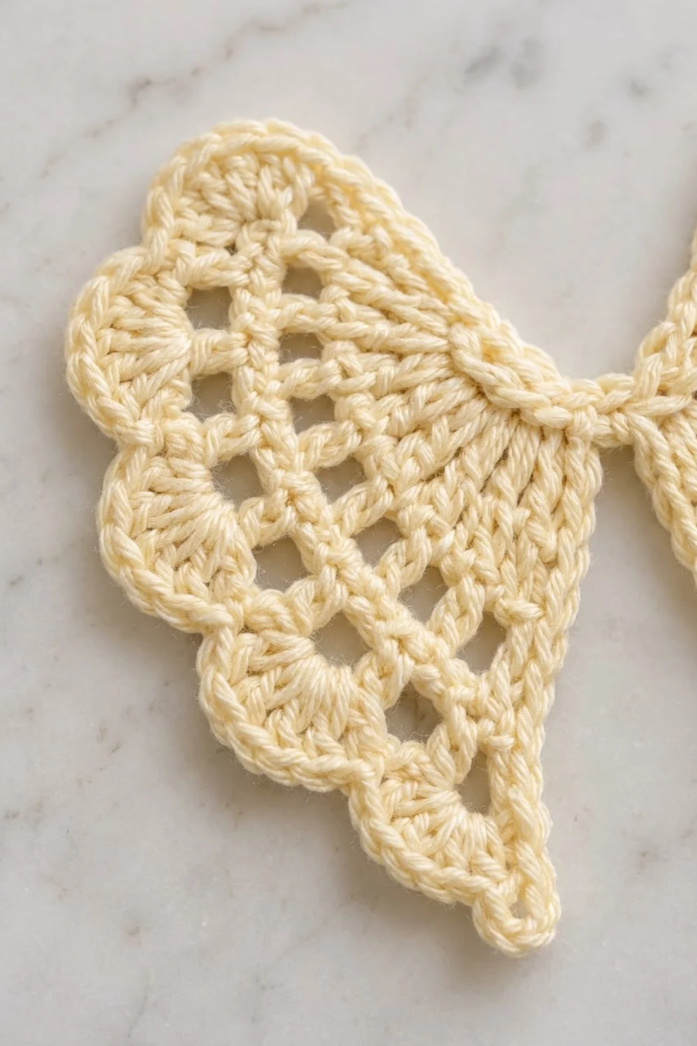 Cream-colored crocheted lace motif with open stitch pattern displayed on a light marble surface.