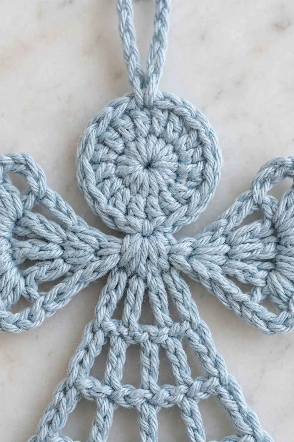 A light blue crocheted snowflake ornament with intricate details hanging against a white marble background.