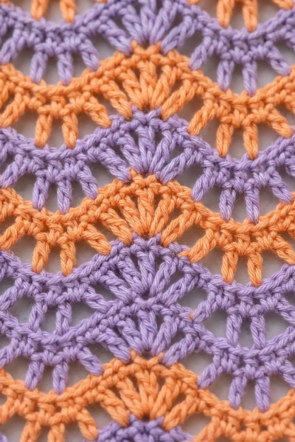 Close-up of purple and orange crocheted fabric showing an interlocking shell stitch pattern with open spaces.
